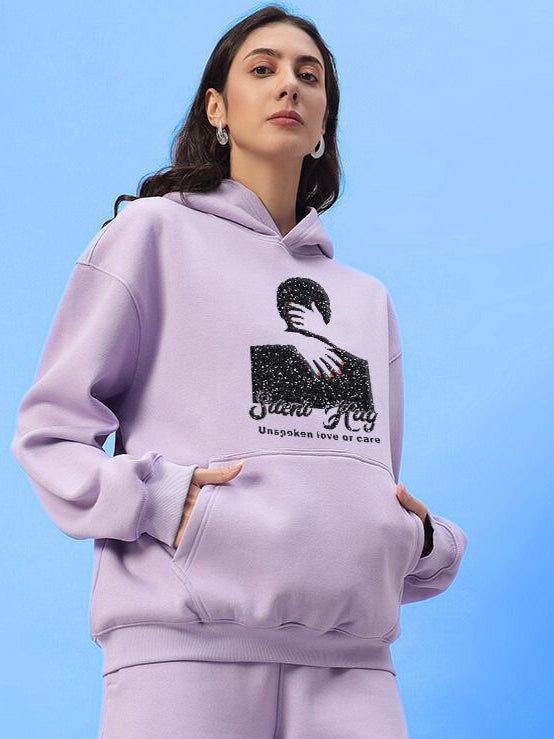 Woman wearing WOMENS SILENT HUG PRINTED FLEECE HOODIE LILAC in soft pastel tone, showcasing modern style with artistic printed detailing.