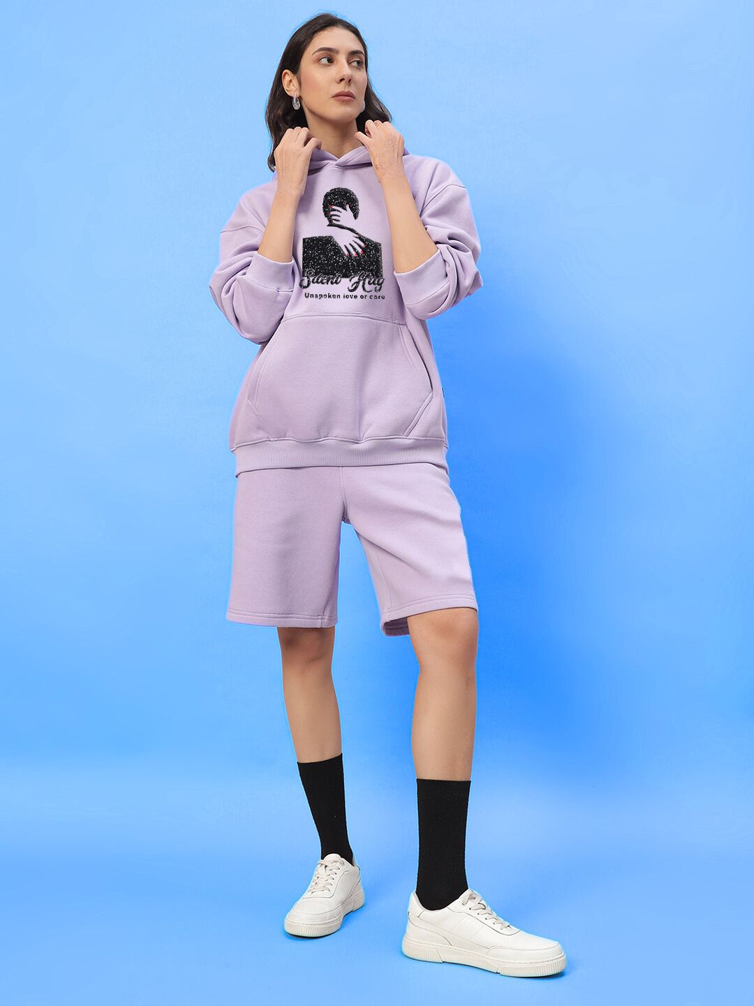 Woman wearing WOMENS SILENT HUG PRINTED FLEECE HOODIE LILAC, styled in a pastel modern fashion.