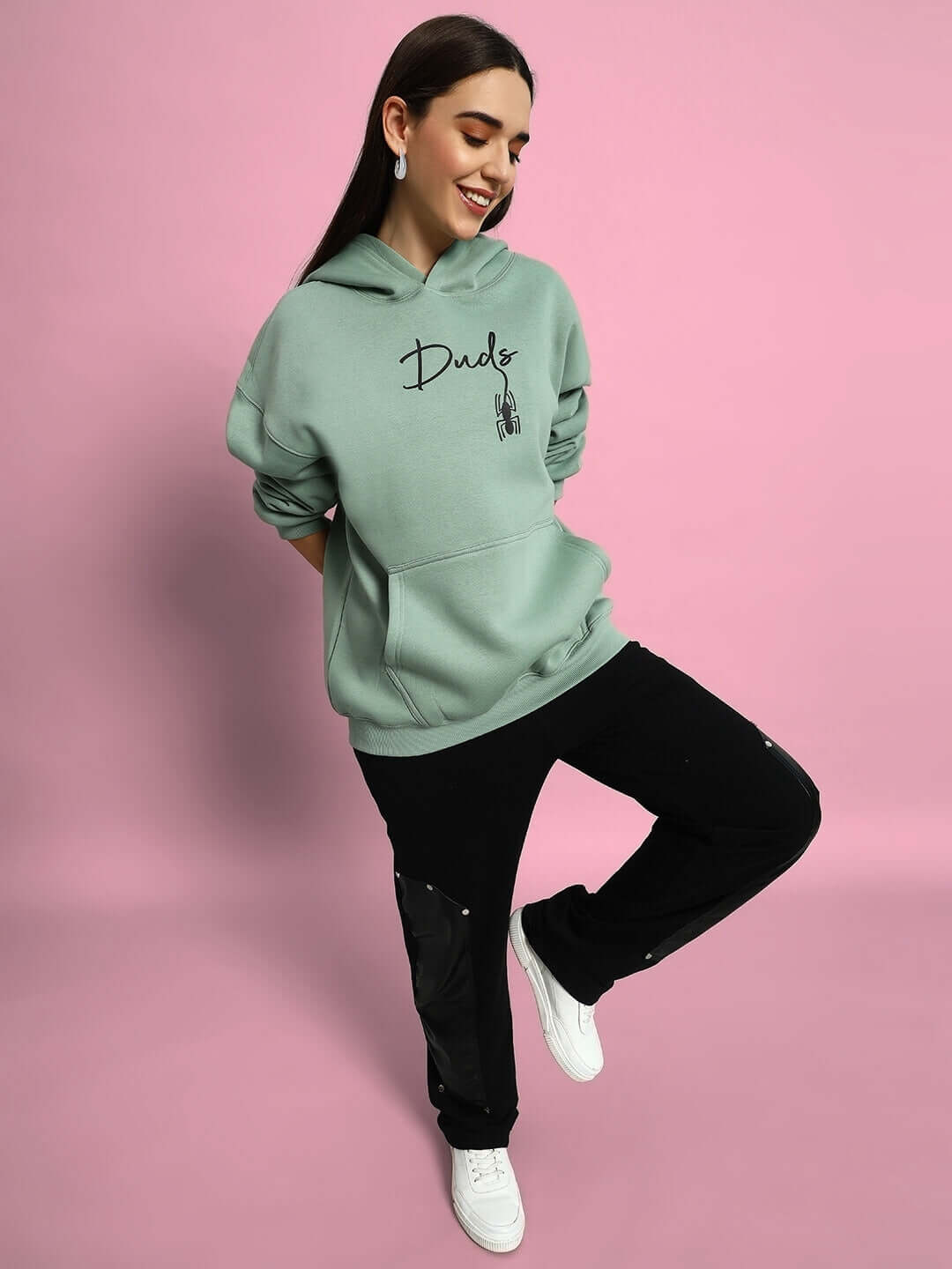 Woman wearing a Women Spiderman Oversized Fleece Hoodie Jade Green with black pants, posing against a pink background.