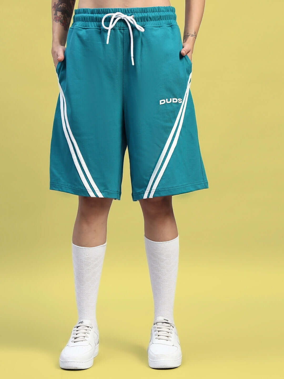 Model wearing teal athletic shorts with white stripes and "DUDS" branding, paired with long white socks and white sneakers.