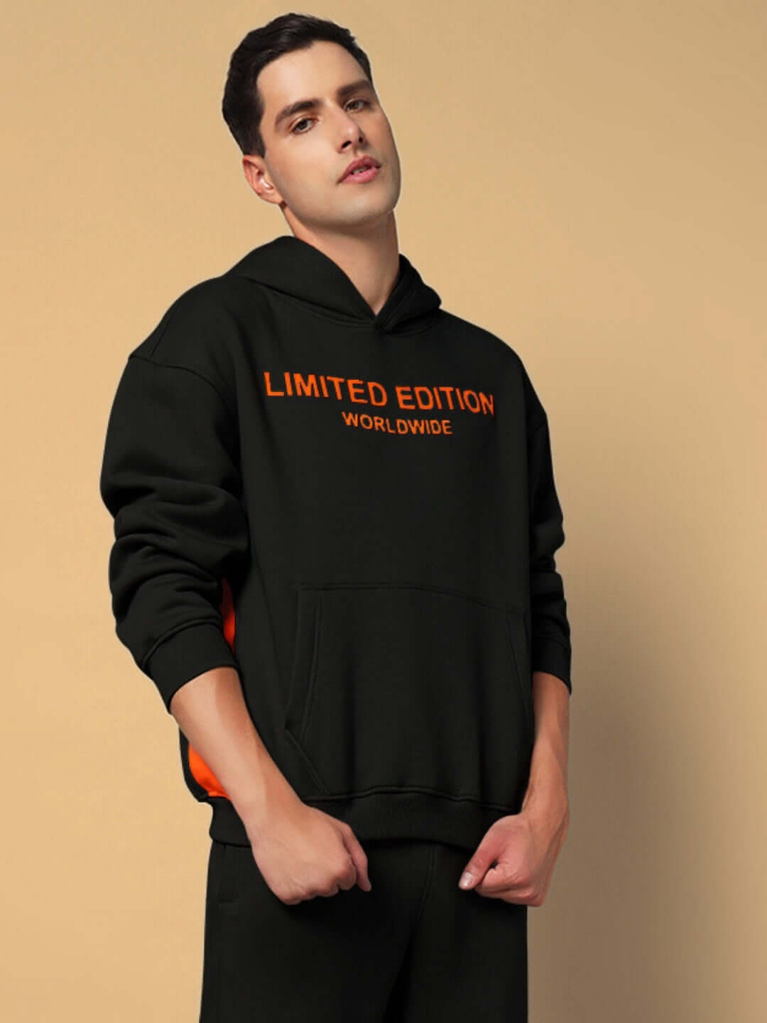 Model wearing WORLDWIDE FLEECE HOODIES BLACK in a stylish pose, showcasing a limited edition design with orange lettering on a black hoodie.