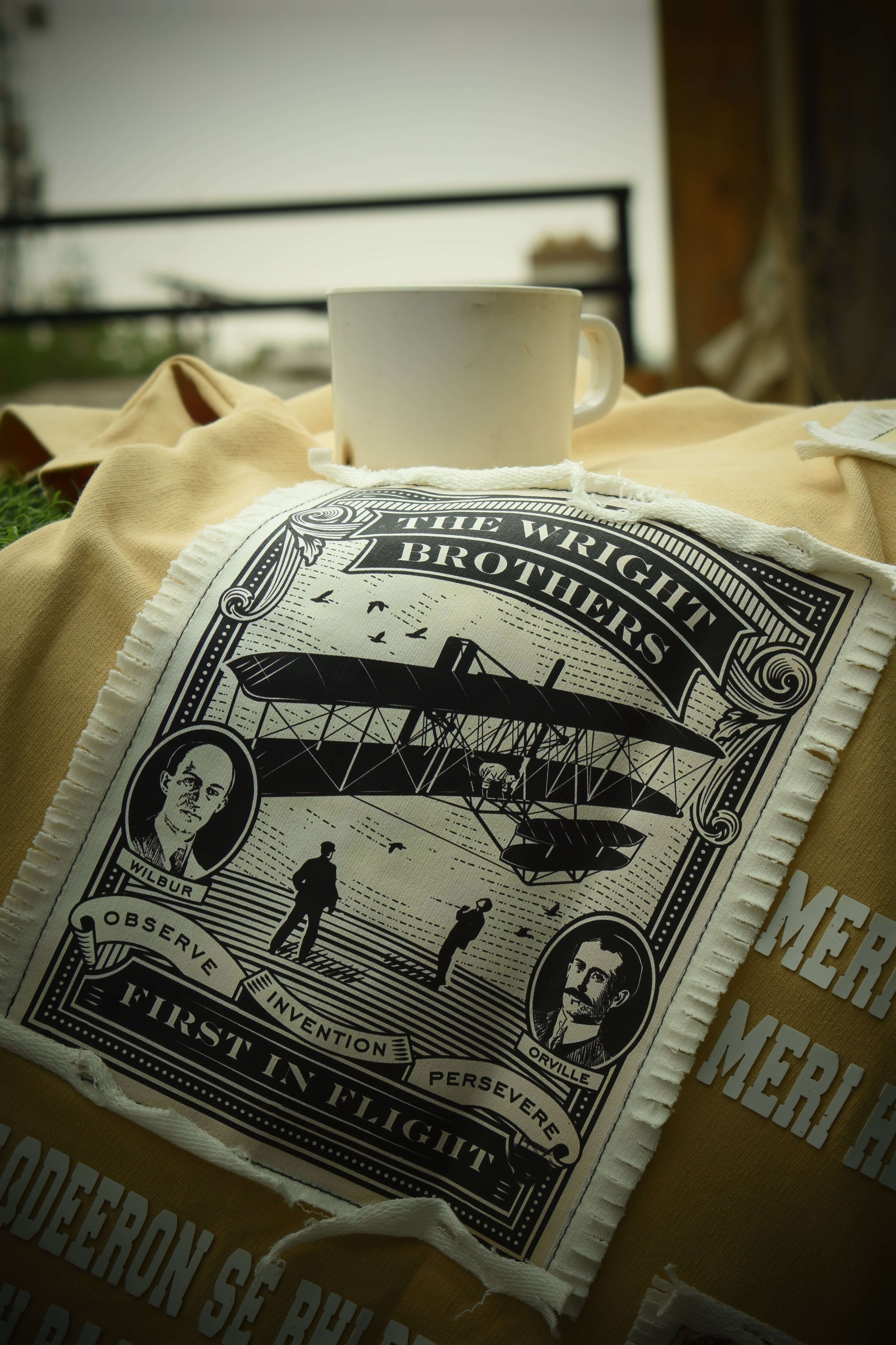 Decorative pillow with vintage Wright Brothers print on beige blanket, accompanied by a white coffee cup outdoors.