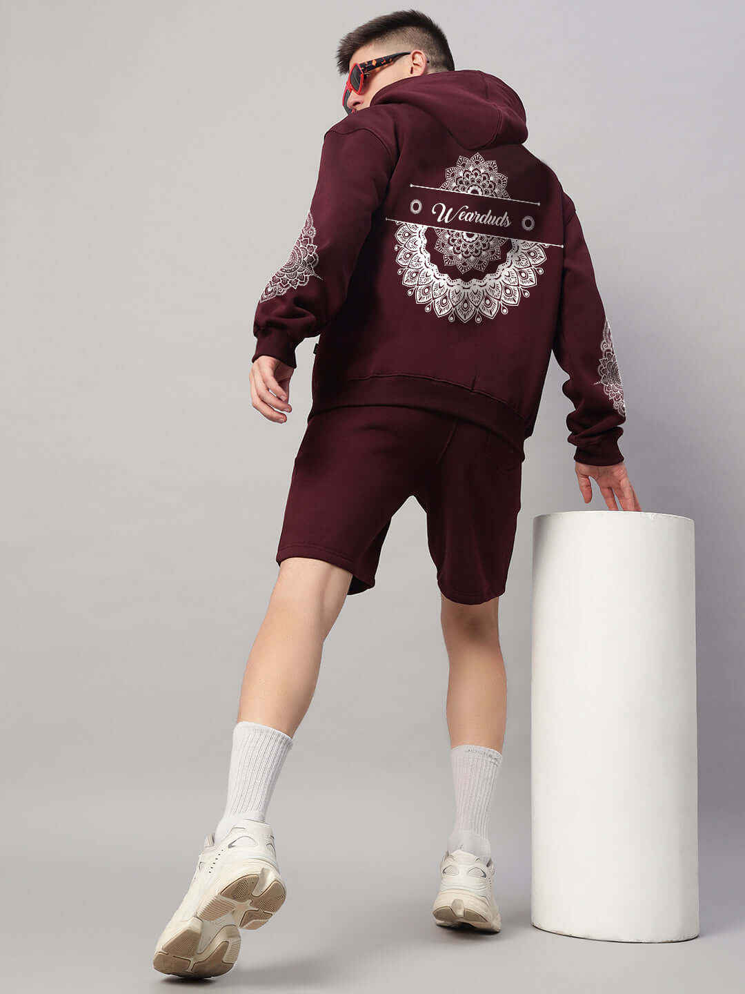 Man wearing WEARDUDS YANTRA FLEECE SHORTS WINE with hoodie, showcasing back design in studio setting.