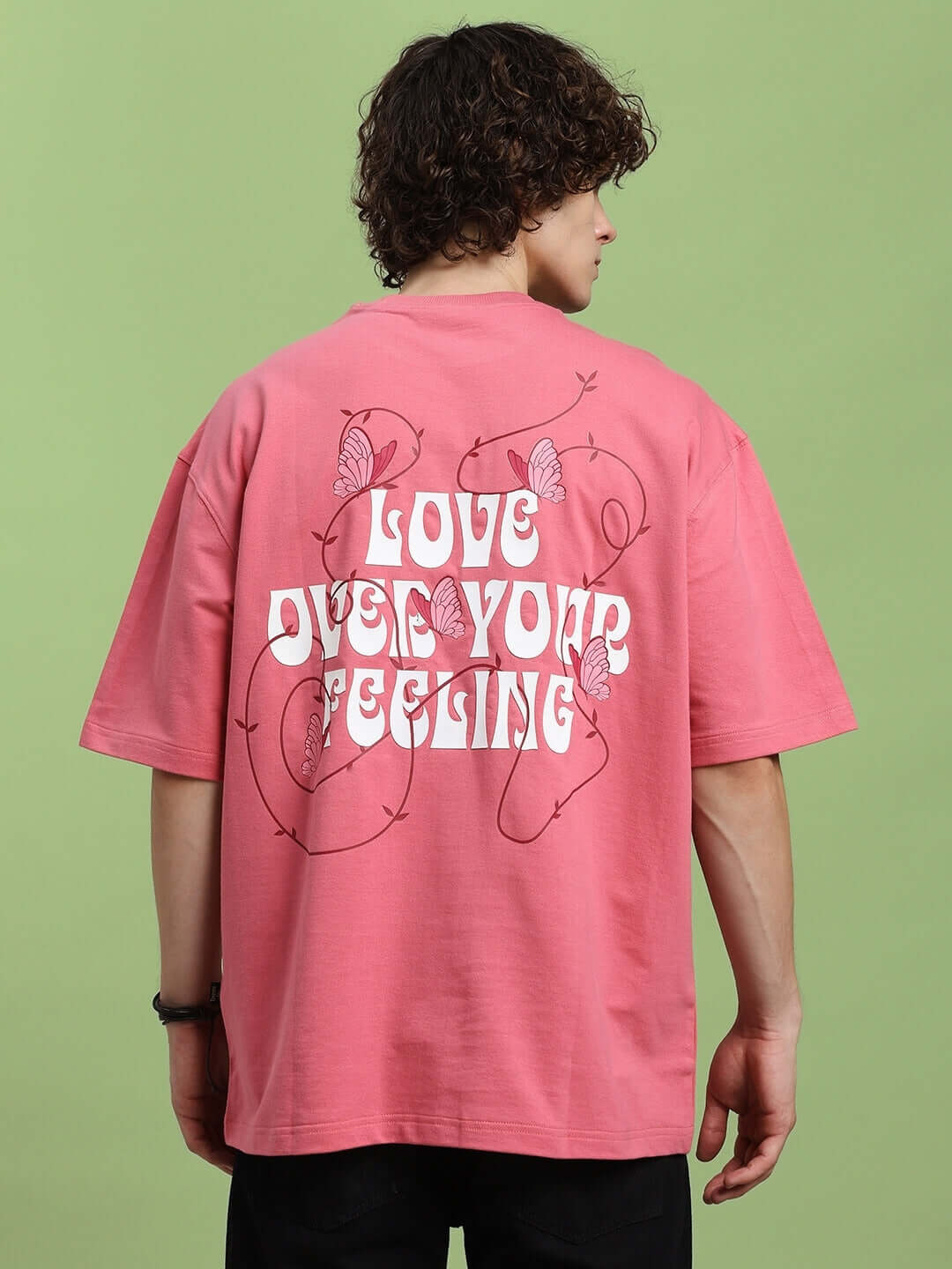 Back view of pink T-shirt with 'LOVE YOUR FEELING' print, made from premium cotton and elastane fabric, worn by a model.