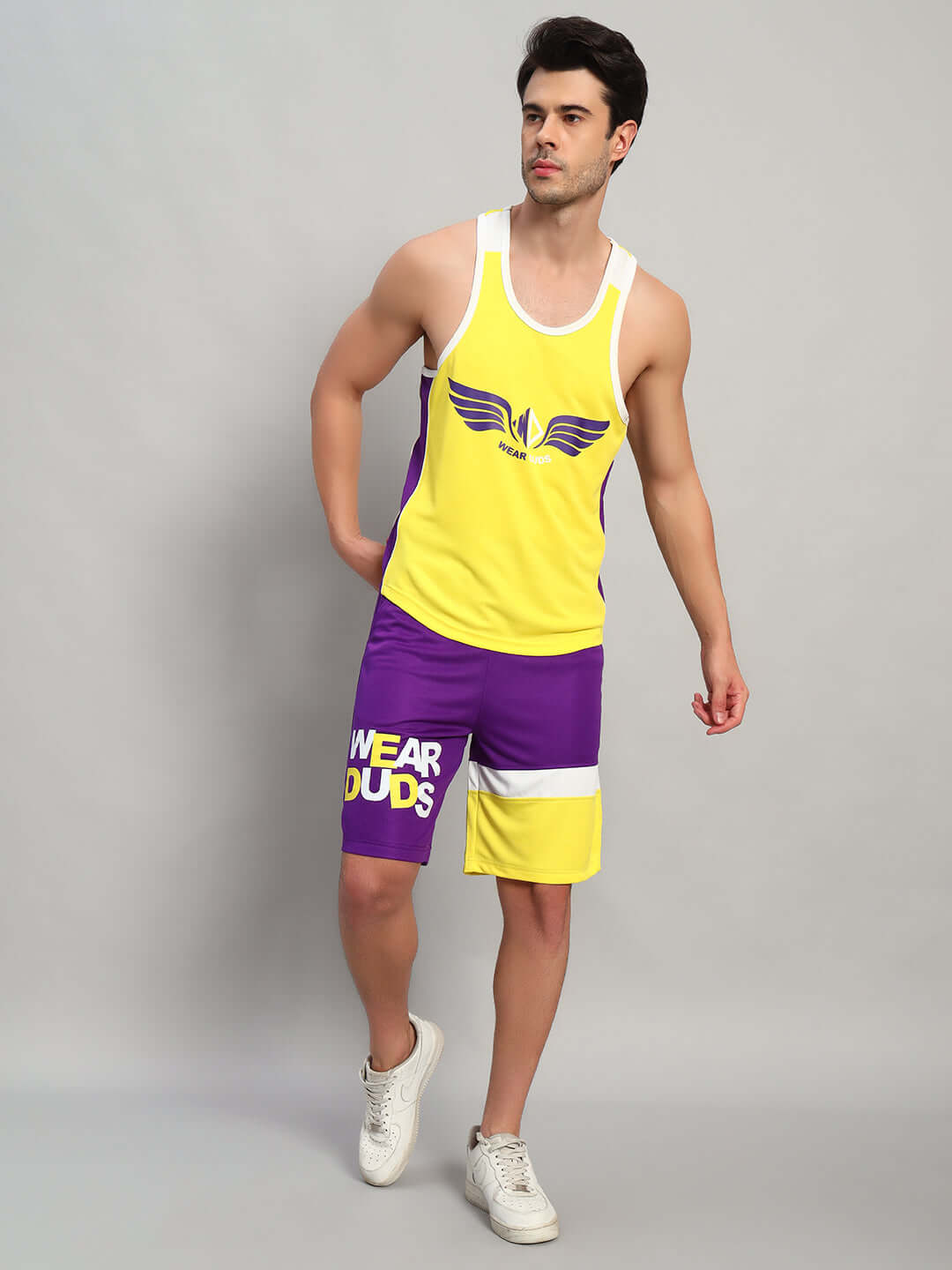 Man wearing ZENITH REGULAR FIT SHORTS PURPLE YELLOW with matching tank top, showcasing athletic style and vibrant color combination.