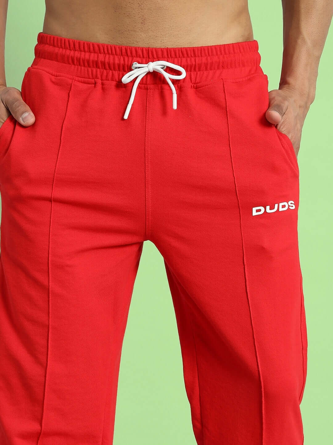 Man wearing red ZION Side Slit Joggers by DUDS, featuring comfortable fit and drawstring waistband on green background.