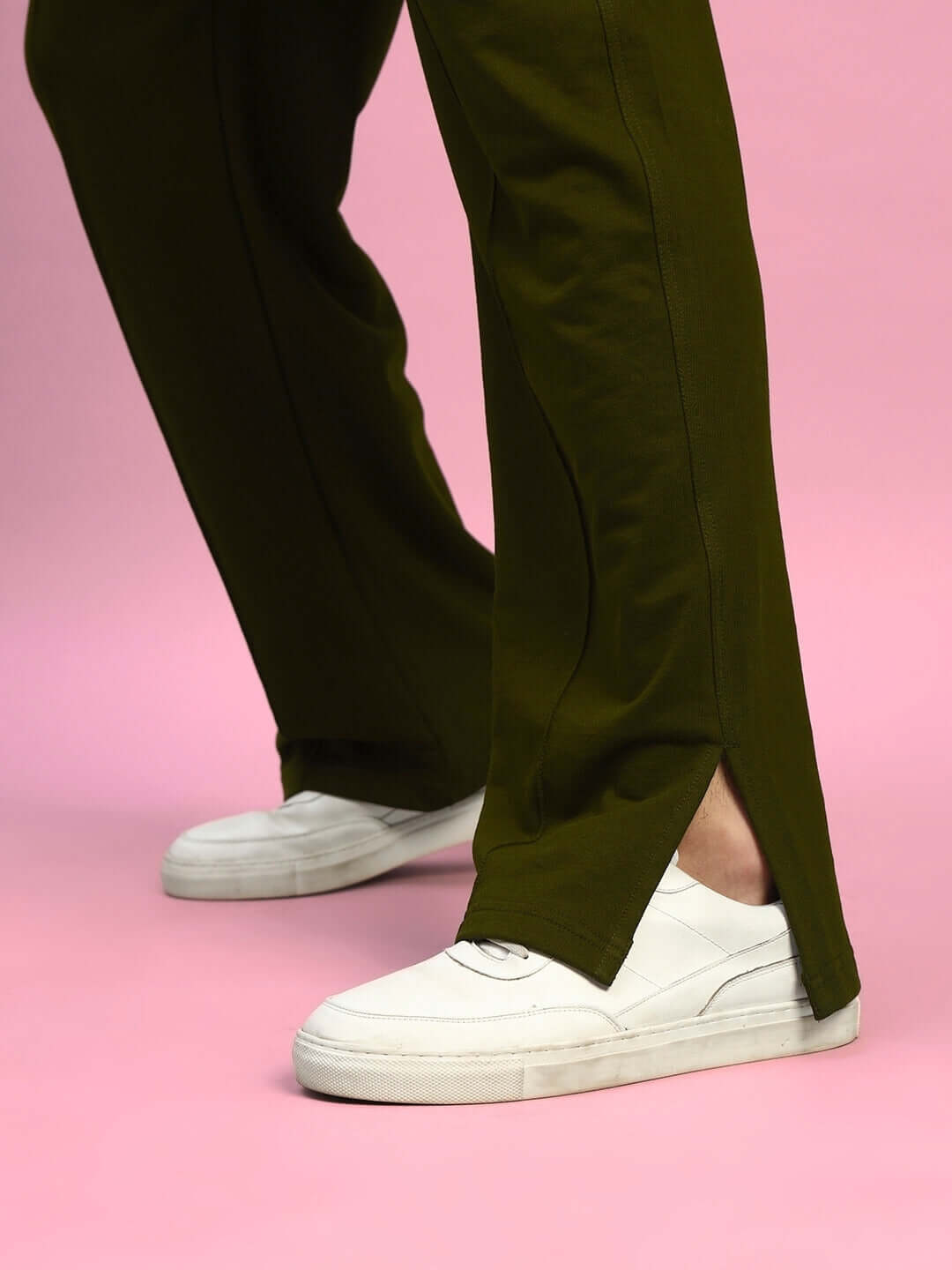 Person wearing olive green Zion relaxed fit joggers with white sneakers against pink background, showing close-up of elasticated waistband.
