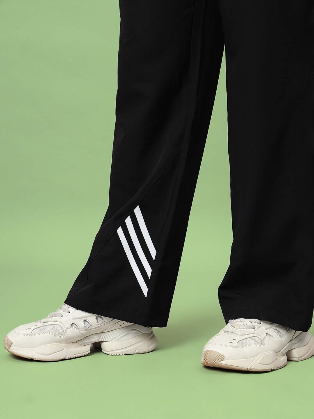 Person wearing black Zoomer relaxed fit cargo pants with white sneakers on a green background.